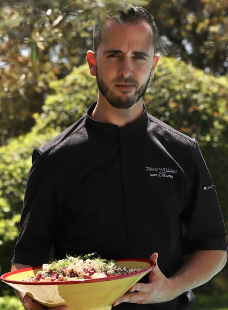 Le chef John William, traiteur, présente un grand bol de salade composée. Veste noire brodée John William Chef Traiteur.